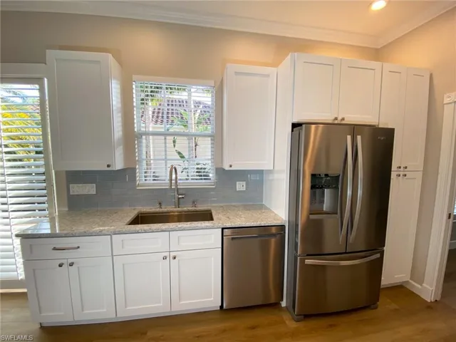 Kitchen featuring stainless steel appliances, white cabinetry, light stone counters, ornamental molding, and dark wood finished floors