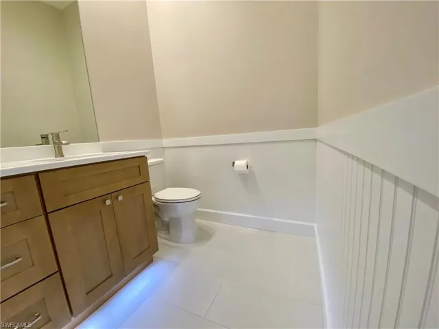 Half bathroom featuring wainscoting, vanity, light tile patterned floors, and a decorative wall