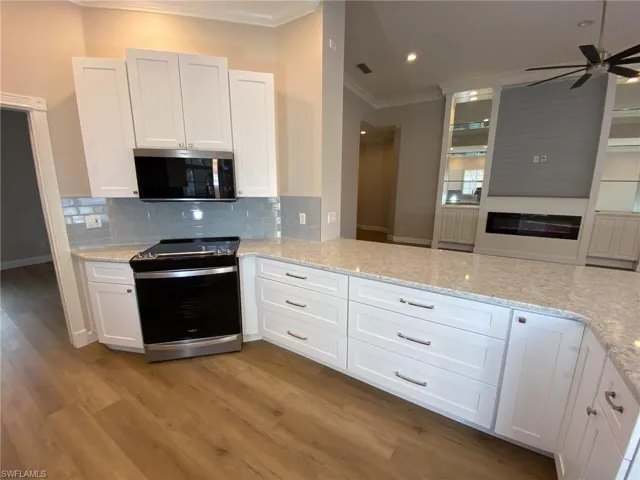 Kitchen featuring white cabinets, stainless steel appliances, light stone countertops, and crown molding