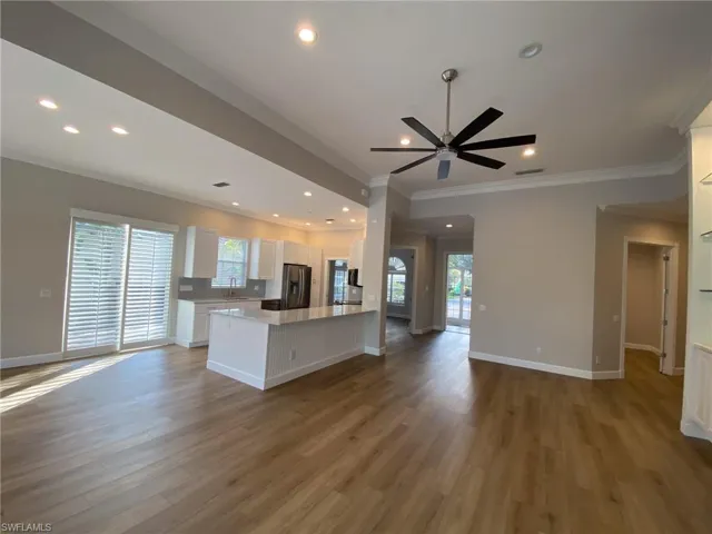 Kitchen with open floor plan, white cabinetry, ornamental molding, dark wood-type flooring, and stainless steel fridge