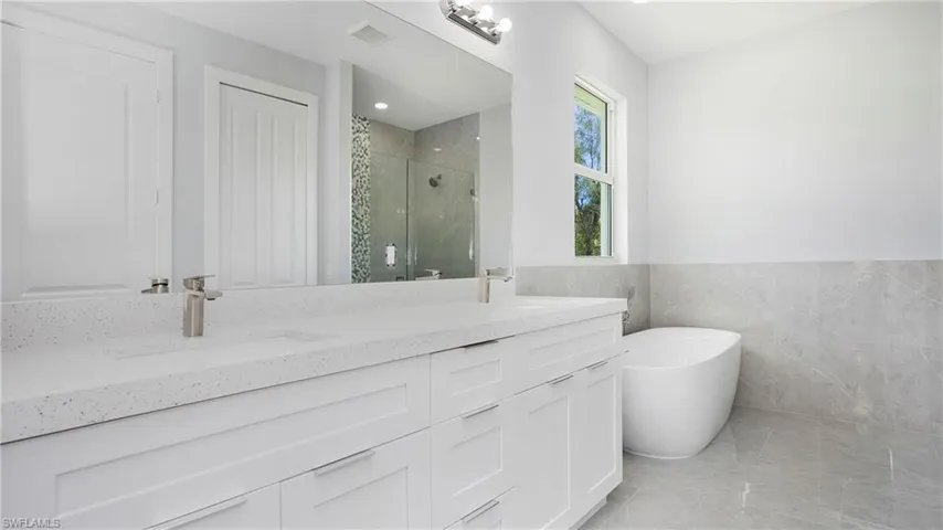 Bathroom with a shower stall, tile walls, double vanity, a freestanding tub, and a wainscoted wall