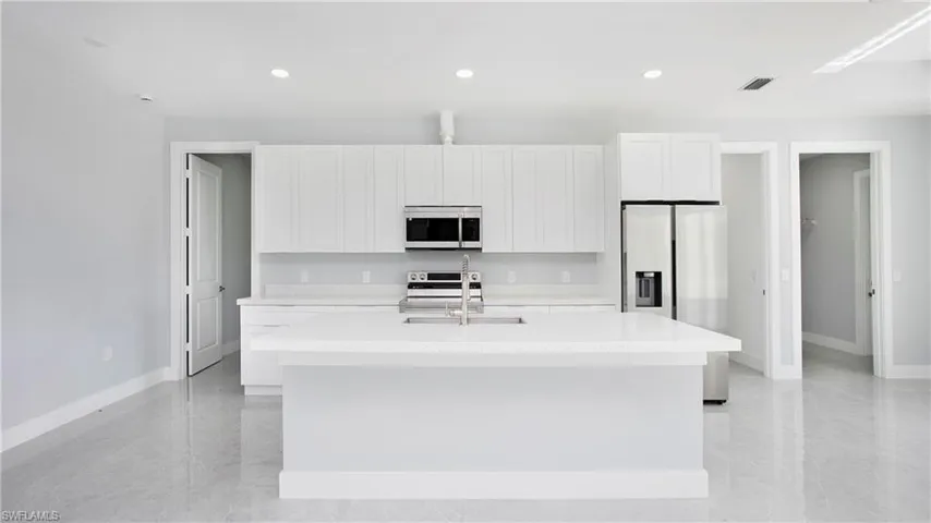 Kitchen featuring an island with sink, white microwave, light countertops, stainless steel fridge with ice dispenser, and white cabinets