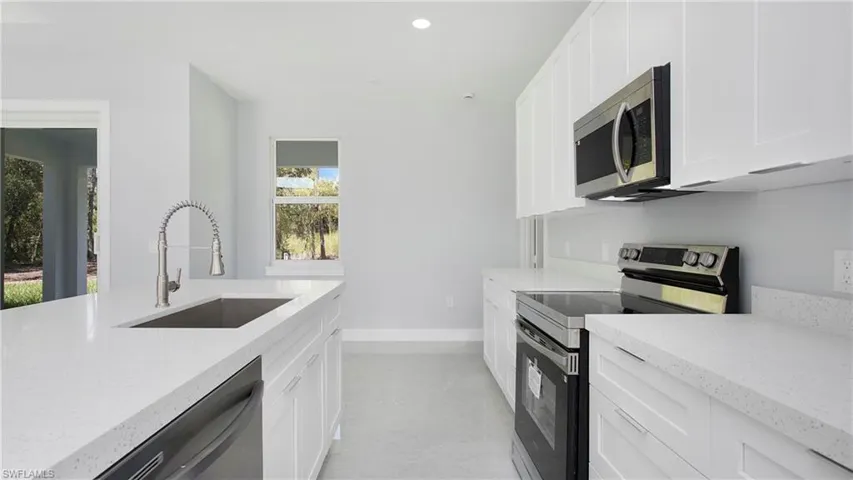 Kitchen with stainless steel appliances, light stone countertops, white cabinetry, and recessed lighting