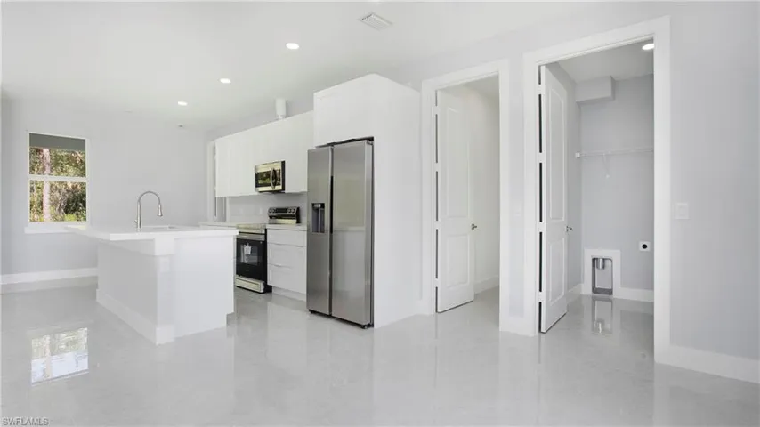 Kitchen with appliances with stainless steel finishes, light countertops, a kitchen island with sink, recessed lighting, and white cabinetry