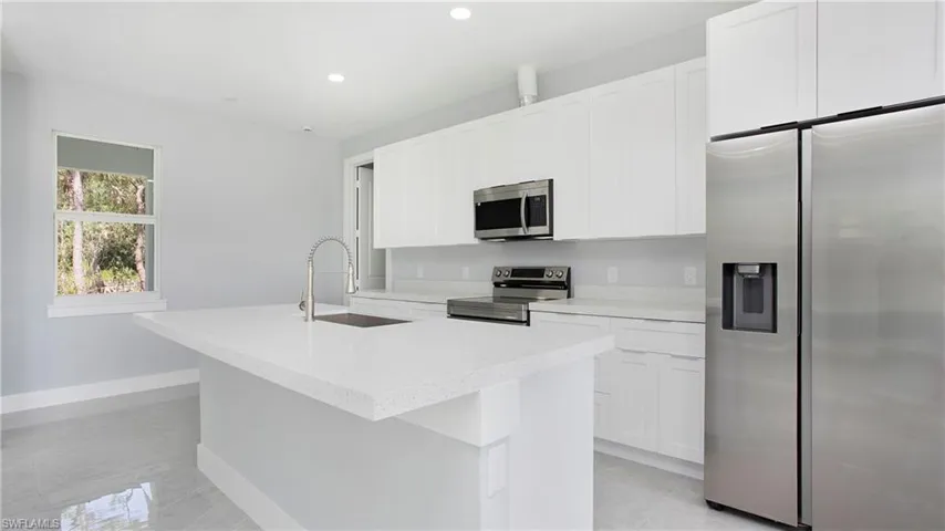 Kitchen featuring stainless steel appliances, an island with sink, white cabinets, light countertops, and recessed lighting