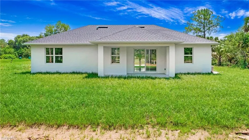 Back of property with stucco siding, a yard, and roof with shingles