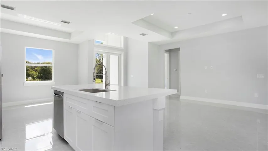 Kitchen featuring a tray ceiling, a center island with sink, white cabinetry, and recessed lighting