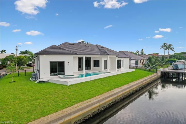 Rear view of house featuring a water view, a swimming pool with hot tub, a lawn, and a patio
