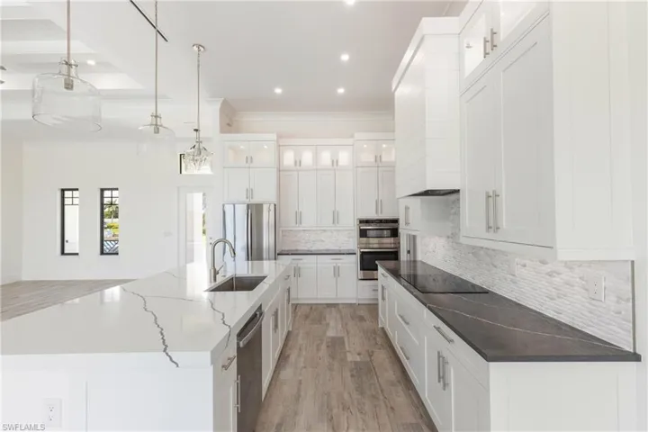 Kitchen featuring decorative light fixtures, stainless steel appliances, sink, a large island, and dark stone counters