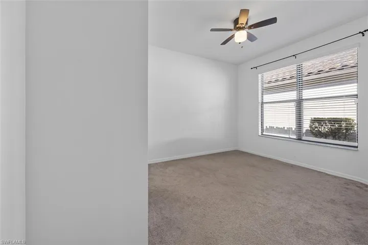 Carpeted spare room featuring a ceiling fan and baseboards