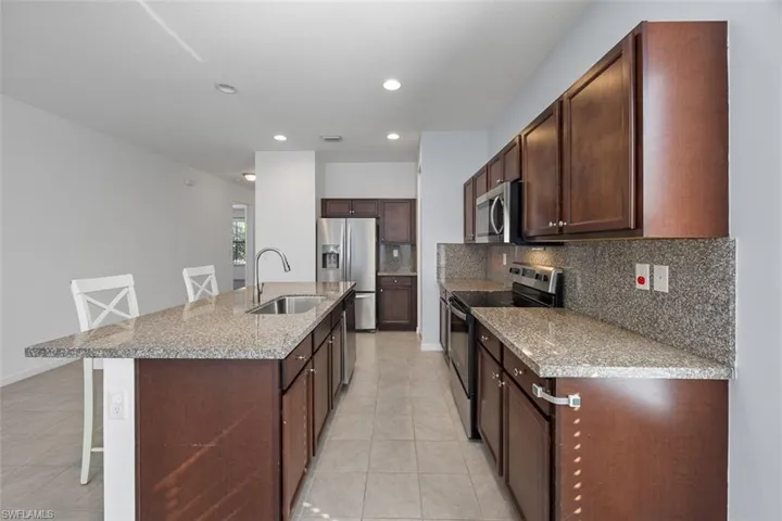 Kitchen with a center island with sink, a sink, appliances with stainless steel finishes, a kitchen breakfast bar, and backsplash