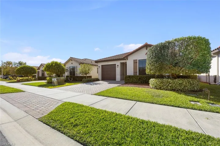 View of front of property featuring a front lawn, a tiled roof, stucco siding, a garage, and driveway