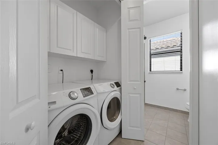 Clothes washing area with cabinet space, light tile patterned floors, separate washer and dryer, and baseboards