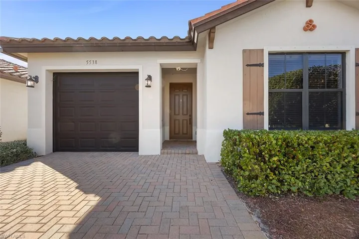View of exterior entry featuring a tiled roof, decorative driveway, a garage, and stucco siding