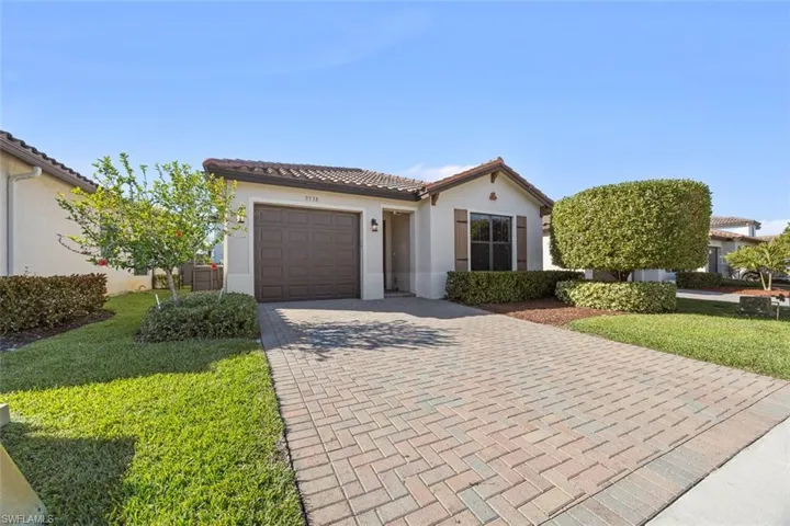 View of front facade featuring a tile roof, decorative driveway, an attached garage, and stucco siding