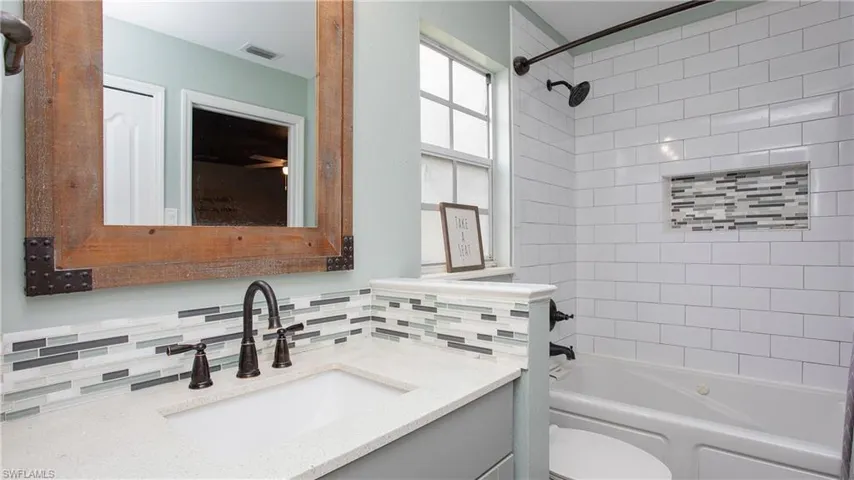 Full bathroom with tasteful backsplash, tiled shower / bath combo, vanity, and toilet