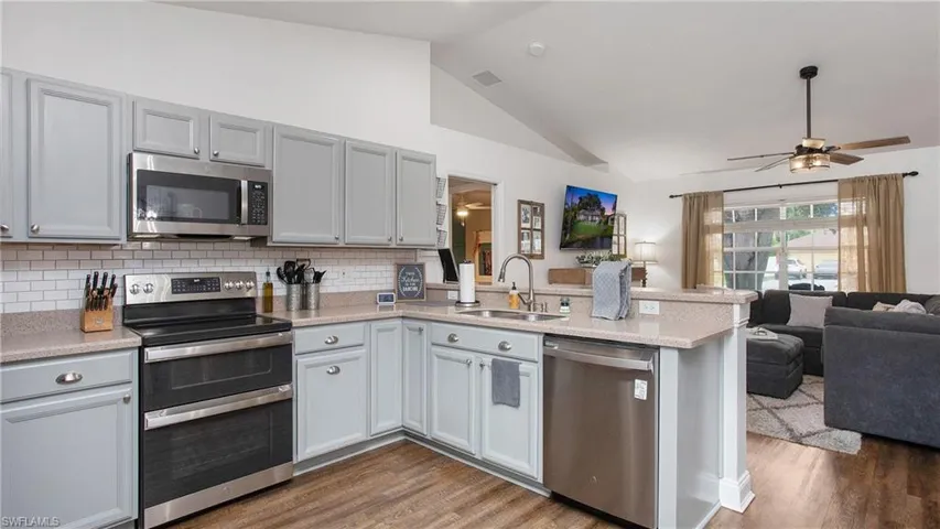 Kitchen with dark hardwood / wood-style flooring, stainless steel appliances, lofted ceiling, ceiling fan, and sink