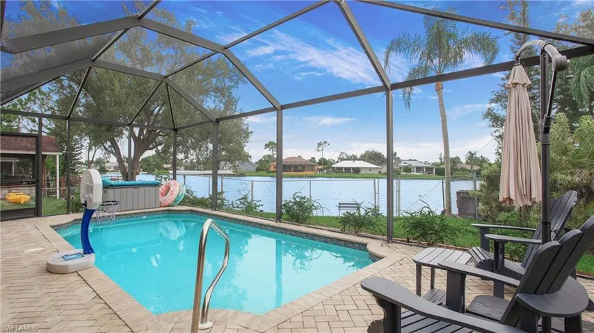 View of pool featuring a patio, a water view, a hot tub, and glass enclosure