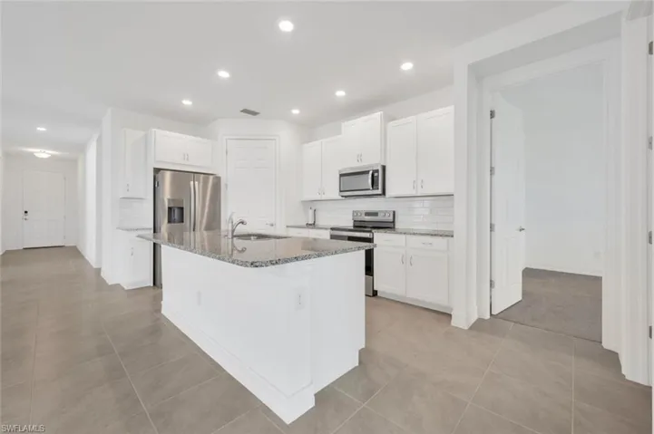 Kitchen featuring backsplash, appliances with stainless steel finishes, white cabinets, light stone countertops, and recessed lighting