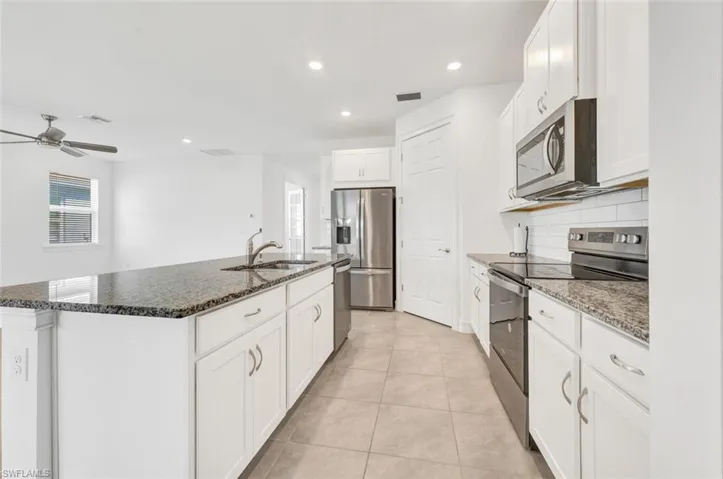 Kitchen featuring stainless steel appliances, a kitchen island with sink, dark stone countertops, recessed lighting, and white cabinetry