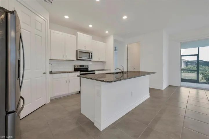 Kitchen with stainless steel appliances, white cabinetry, dark stone counters, a kitchen island with sink, and decorative backsplash