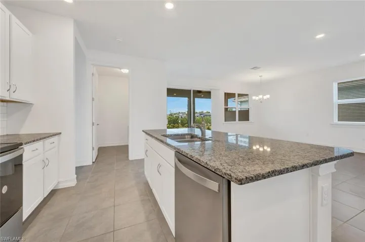 Kitchen featuring white cabinetry, dark stone countertops, appliances with stainless steel finishes, recessed lighting, and an island with sink