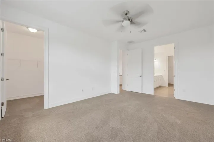 Unfurnished bedroom with a walk in closet, light carpet, a ceiling fan, and ensuite bath