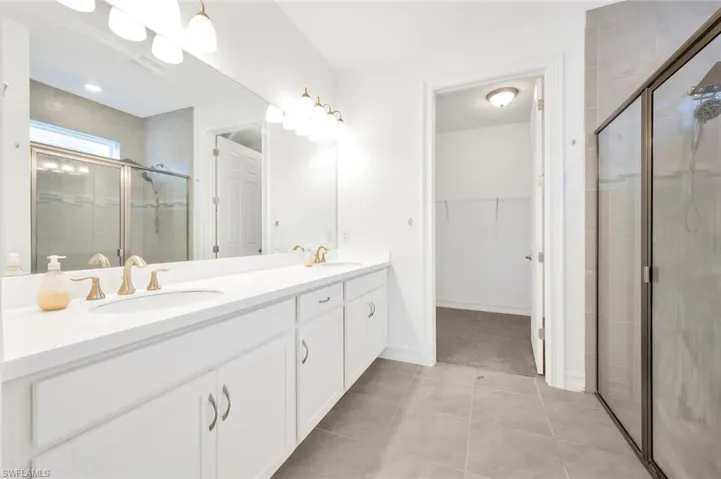 Full bathroom with double vanity, a shower stall, a walk in closet, and light tile patterned floors