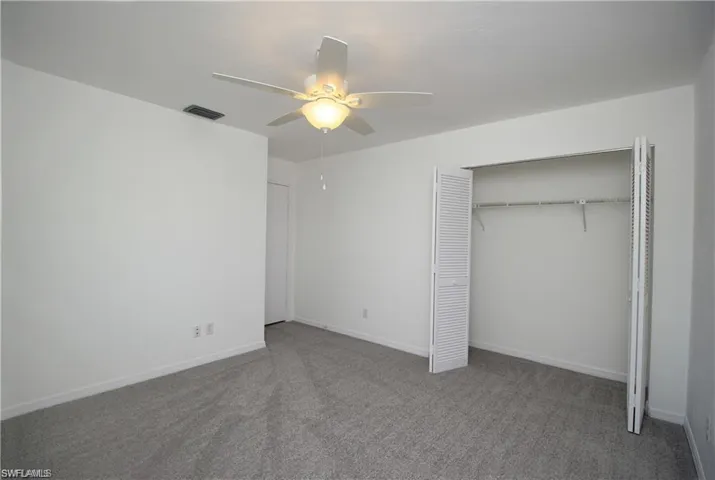 Unfurnished bedroom featuring a closet, ceiling fan, and dark carpet