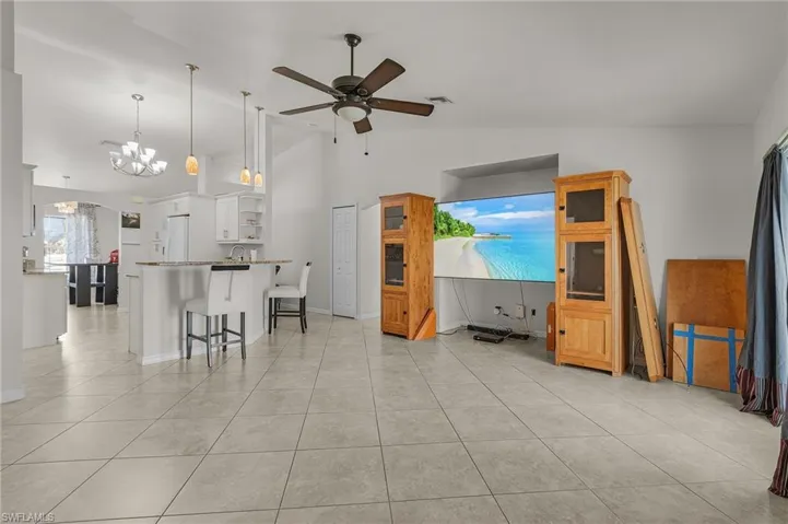 Living room featuring ceiling fan with notable chandelier, vaulted ceiling, visible vents, and light tile patterned floors