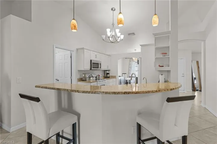 Kitchen with white electric range, an inviting chandelier, stainless steel microwave, light tile patterned flooring, and a kitchen bar