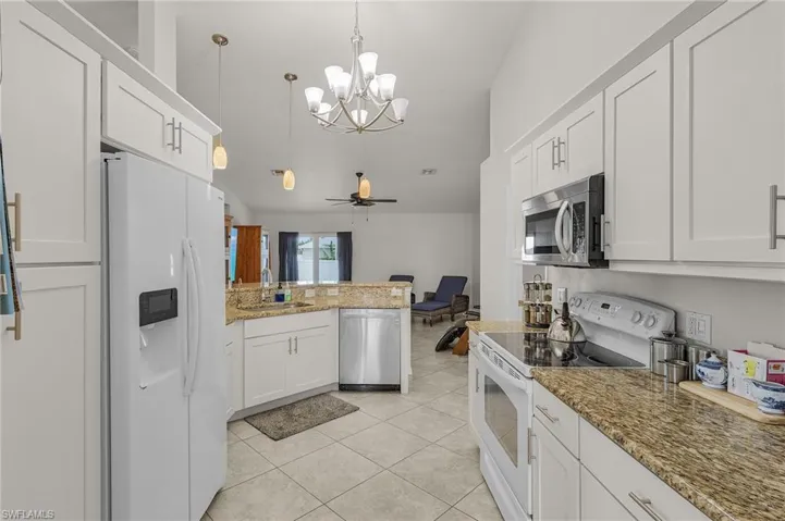 Kitchen featuring a sink, light tile patterned floors, stainless steel appliances, a peninsula, and lofted ceiling