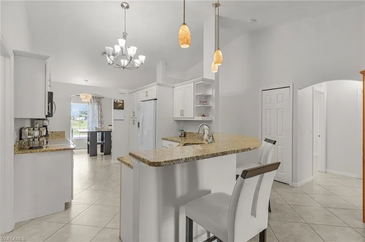 Kitchen with arched walkways, light tile patterned flooring, a sink, and white refrigerator with ice dispenser