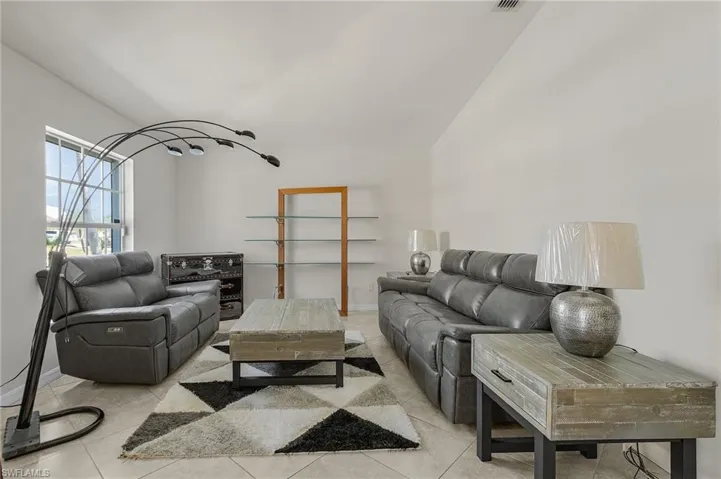 Living area with baseboards, light tile patterned flooring, and vaulted ceiling