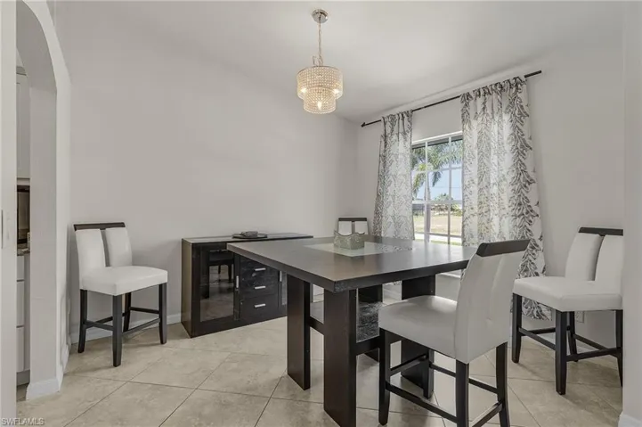 Dining area with baseboards, arched walkways, a notable chandelier, and light tile patterned floors