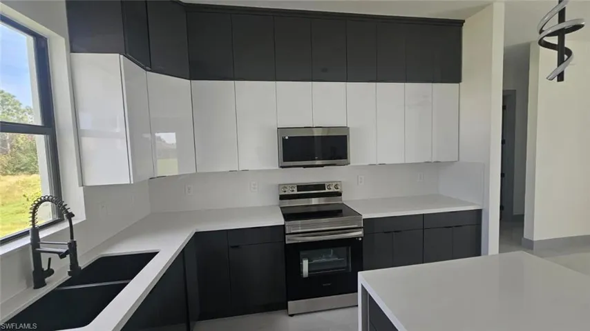 Kitchen with appliances with stainless steel finishes, white cabinets, sink, and plenty of natural light