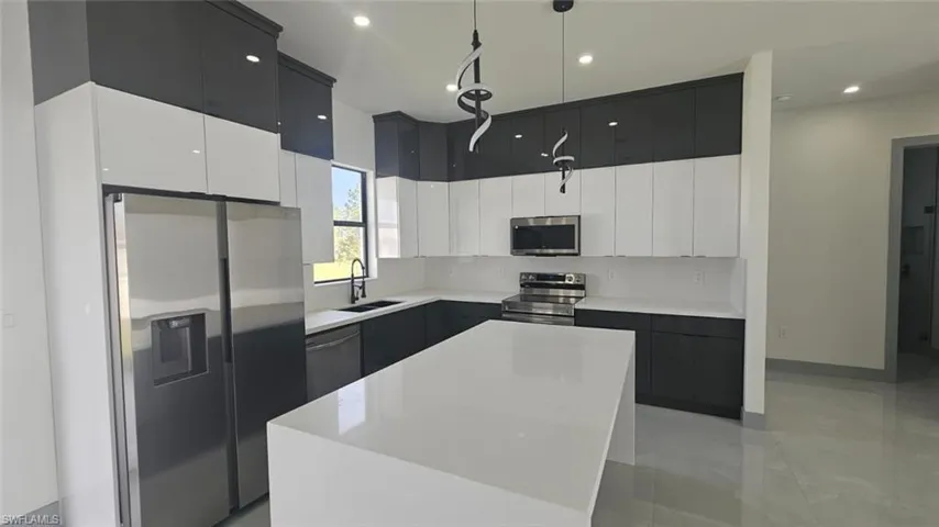 Kitchen featuring white cabinets, a kitchen island, stainless steel appliances, sink, and decorative light fixtures