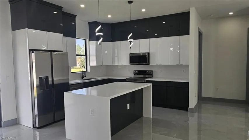 Kitchen with a kitchen island, stainless steel appliances, sink, pendant lighting, and white cabinetry