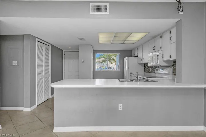 Kitchen featuring light countertops, a peninsula, white appliances, white cabinets, and light tile patterned floors