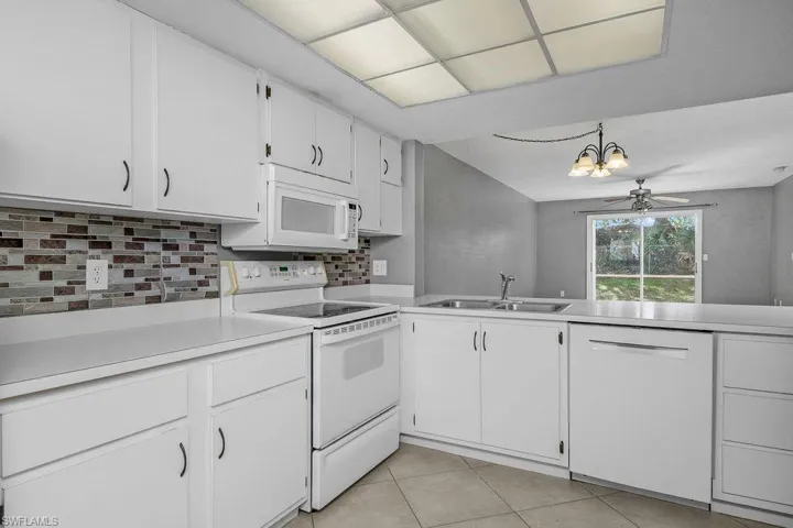 Kitchen with white appliances, white cabinets, light countertops, backsplash, and a chandelier