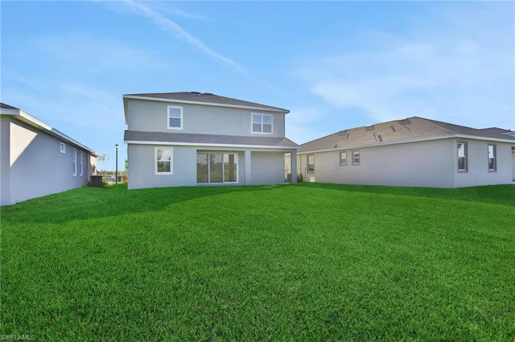 Back of house featuring stucco siding, a lawn, and a patio