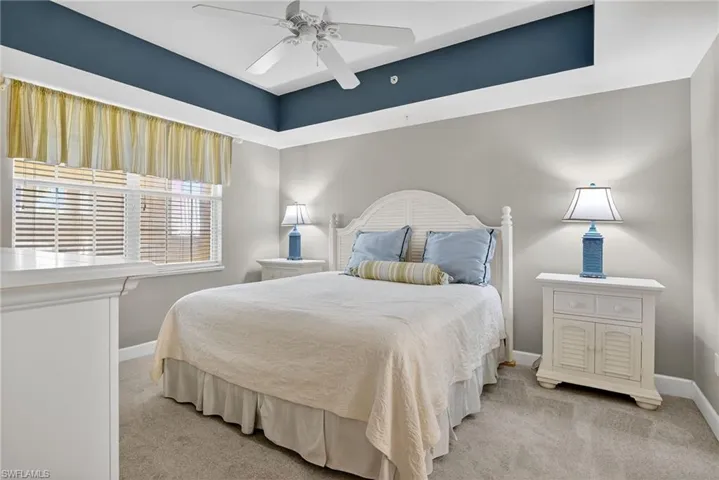 Bedroom featuring light colored carpet, a tray ceiling, and ceiling fan