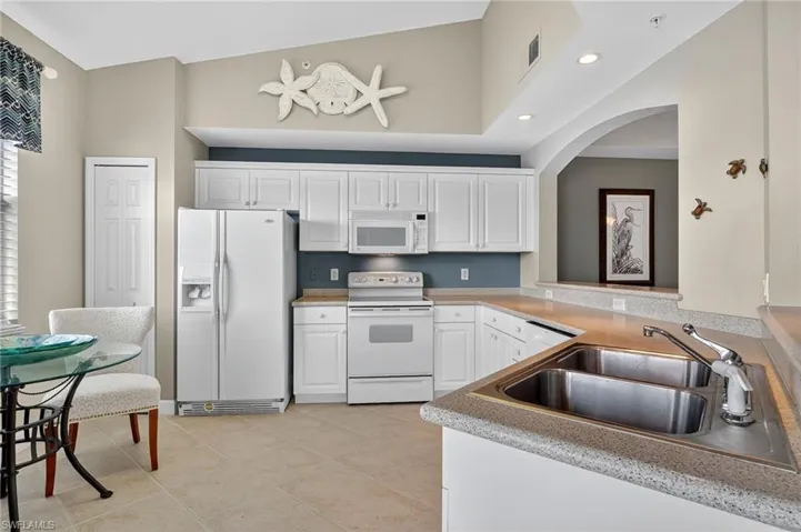 Kitchen featuring white appliances, white cabinets, light countertops, recessed lighting, and light tile patterned flooring