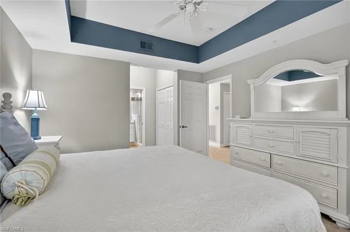 Bedroom with a ceiling fan, a raised ceiling, connected bathroom, and a closet