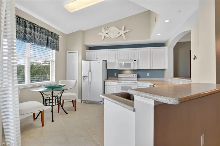 Kitchen featuring white appliances, white cabinetry, a peninsula, recessed lighting, and light tile patterned floors