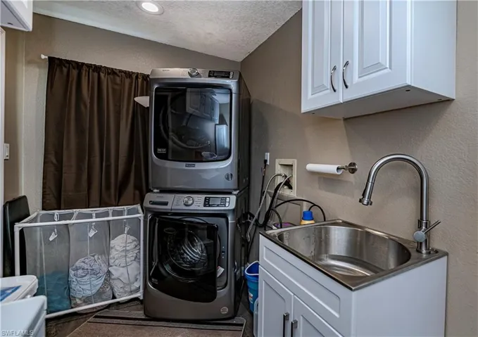 Laundry room with sink, a textured ceiling, and stacked washer and dryer