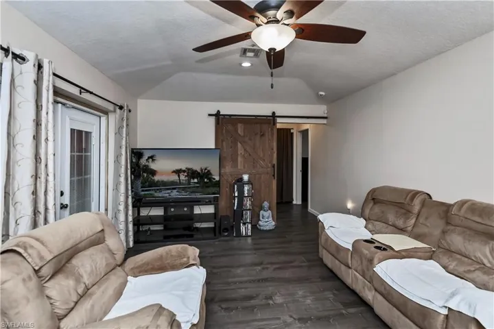Living room featuring ceiling fan, dark hardwood / wood-style floors, a textured ceiling, lofted ceiling, and a barn door
