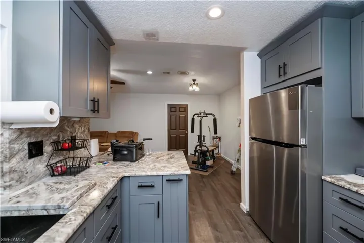 Kitchen featuring dark hardwood / wood-style floors, a textured ceiling, backsplash, stainless steel fridge, and gray cabinetry