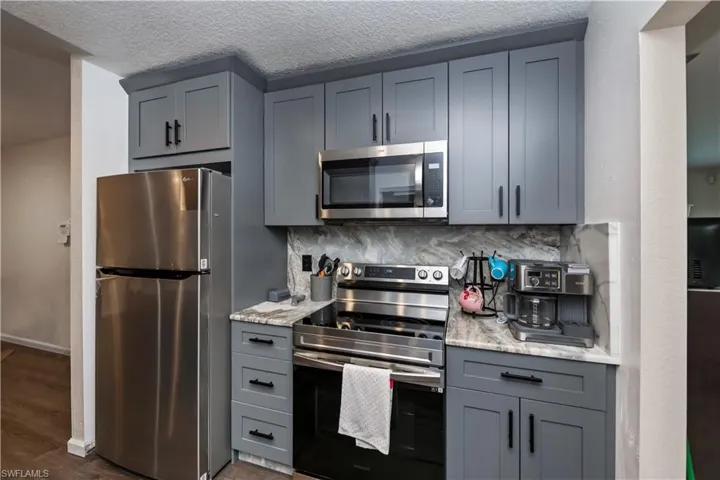Kitchen with decorative backsplash, stainless steel appliances, dark wood-type flooring, and light stone counters