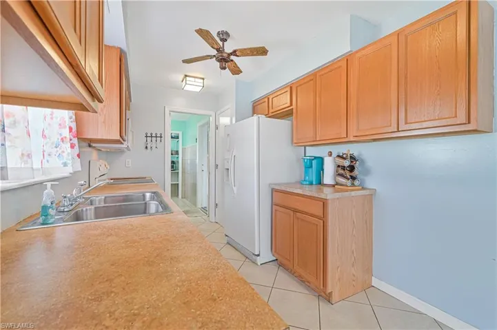 Kitchen featuring white refrigerator with ice dispenser, sink, light tile patterned floors, and ceiling fan